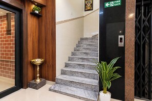 A staircase with a fire exit sign, a potted plant, and a brass water dispenser. - FabHotel Rahul International (Hyderabad)
