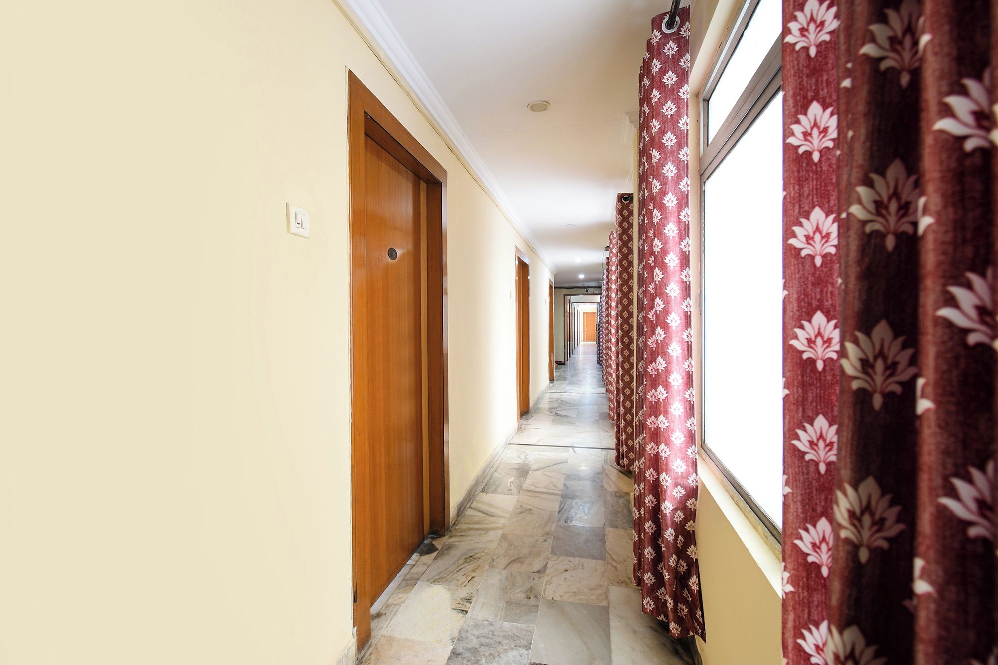 A hallway with a marble floor, wooden doors, and red floral curtains.