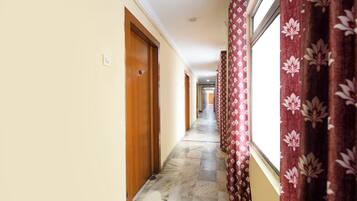 A hallway with a marble floor, wooden doors, and red floral curtains.