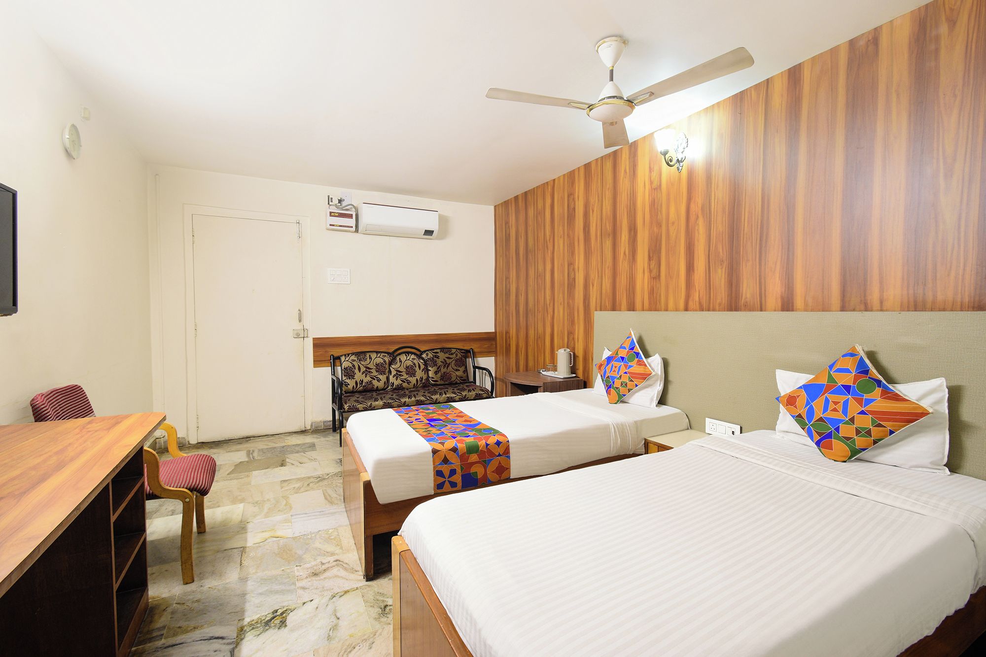 Habitación de hotel con dos camas, un escritorio, una silla, un ventilador de techo y un panel de pared de madera.