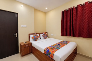 A hotel room with a bed, a nightstand, a door, and a red curtain.