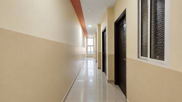 Un pasillo con puertas a un lado y ventanas al otro, que conduce a una habitación luminosa.