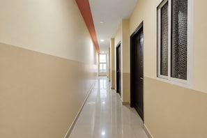A corridor with doors on one side and windows on the other, leading to a bright room.
