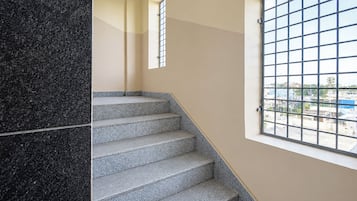 Una escalera con piso estampado que conduce a un rellano, una ventana con celosía metálica y vistas de edificios.