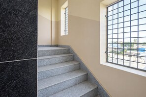 A staircase with a patterned floor leading to a landing, a window with a metal grid, and a view of buildings outside.