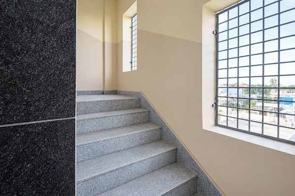 A staircase with a patterned floor leading to a landing, a window with a metal grid, and a view of buildings outside.