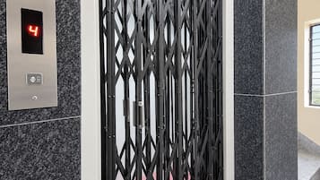 Un ascensor con una pantalla digital que muestra el número 4, un panel metálico con un botón y una puerta metálica negra.
