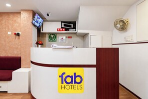 A reception area with a reception desk, a flat-screen TV, a security camera, a no-smoking sign, and a fan on the wall.
