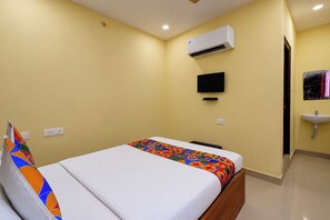 A hotel room with a bed, a television, an air conditioning unit, a sink, and a door.