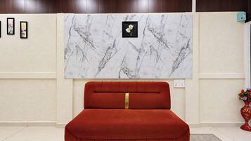 Quarto com cama estofada em vermelho, arte de parede com padrão marmorizado e pequeno vaso vermelho com flores.