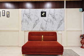 A room with a red upholstered bed, a marble-patterned wall art, and a small red vase with flowers.