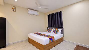 Quarto com cama, ventilador de teto, aparelho de ar condicionado e cortina escura.
