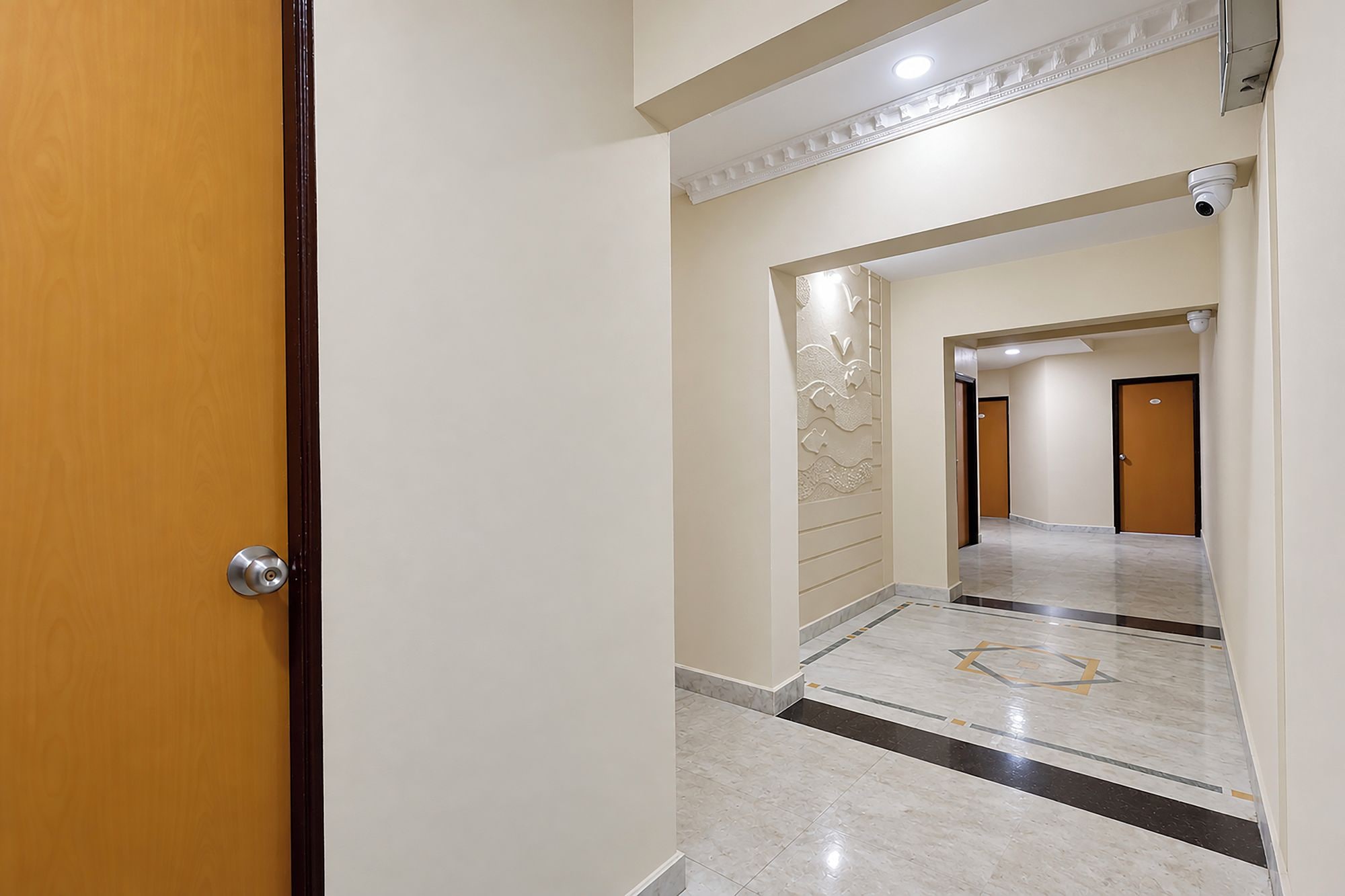 Corredor com porta de madeira, piso de mármore e painel decorativo na parede.