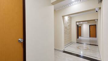 Corredor com porta de madeira, piso de mármore e painel decorativo na parede.