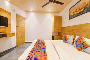 Habitación de hotel con una cama, televisión montada en la pared, ventilador de techo y un cuadro.