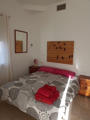 Ein Schlafzimmer mit einem Bett, einem Nachttisch, einem Wandbild und einem Spiegel.
