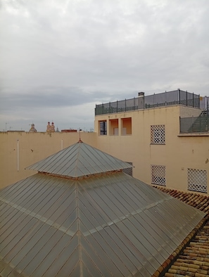Eine Dachterrasse mit wellenförmigem Metalldach und ein helles Gebäude mit zahlreichen Fenstern und einem Metallzaun.