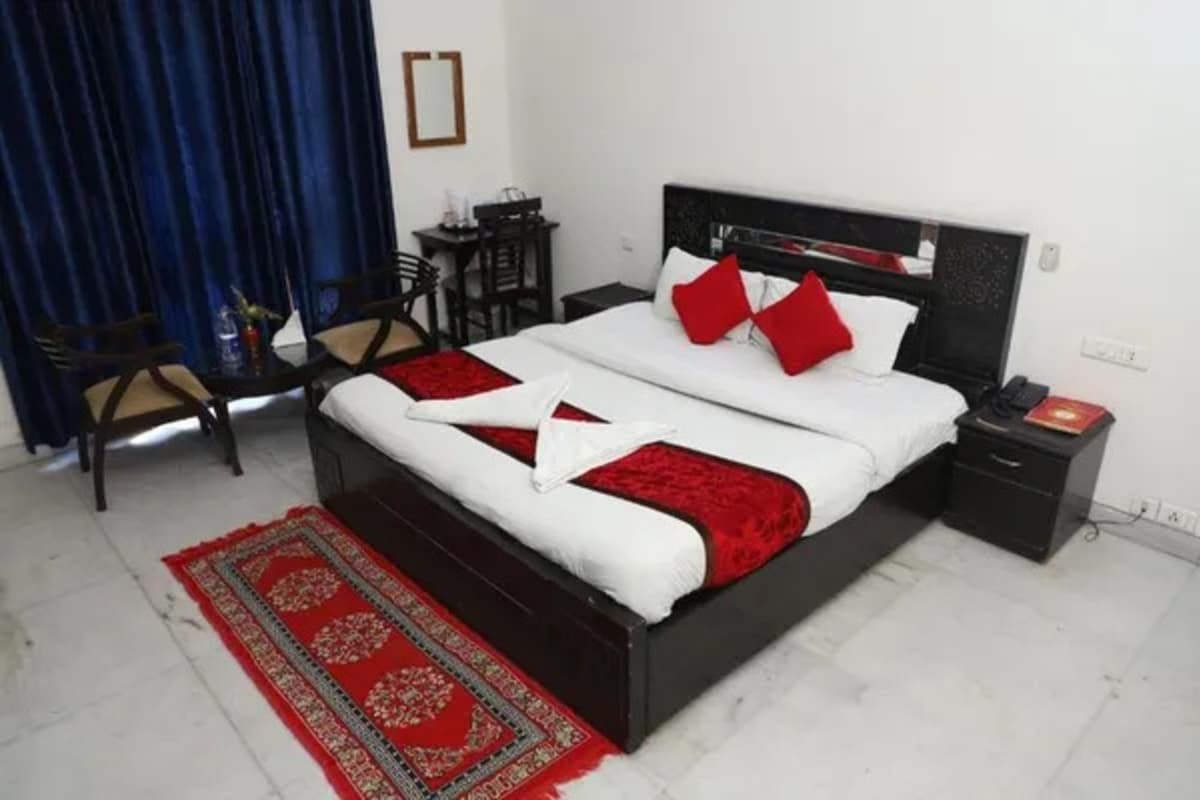 Un lit bien fait, recouvert d’une couverture rouge et blanche, une table de chevet avec une lampe et une chaise.