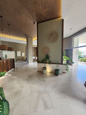 A spacious lobby with a reception desk, decorative wall art, and potted plants.
