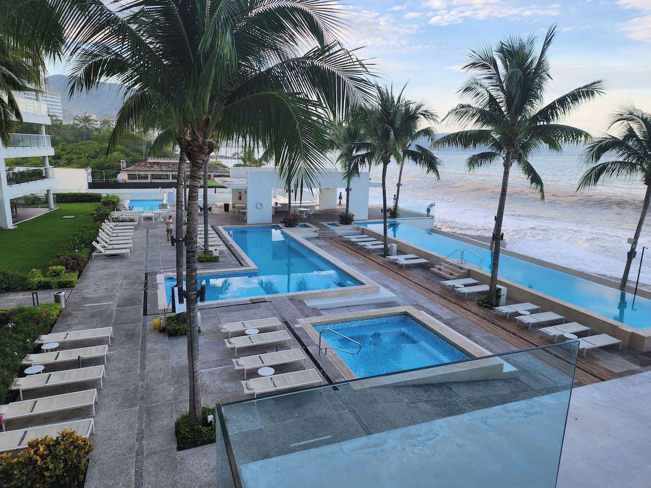 A resort with multiple swimming pools, palm trees, and a view of the beach.