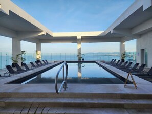 A modern infinity pool with lounge chairs, a clear view of the sea, and a glass railing.