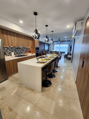 A modern kitchen with a central island, pendant lighting, and a view to the living area.