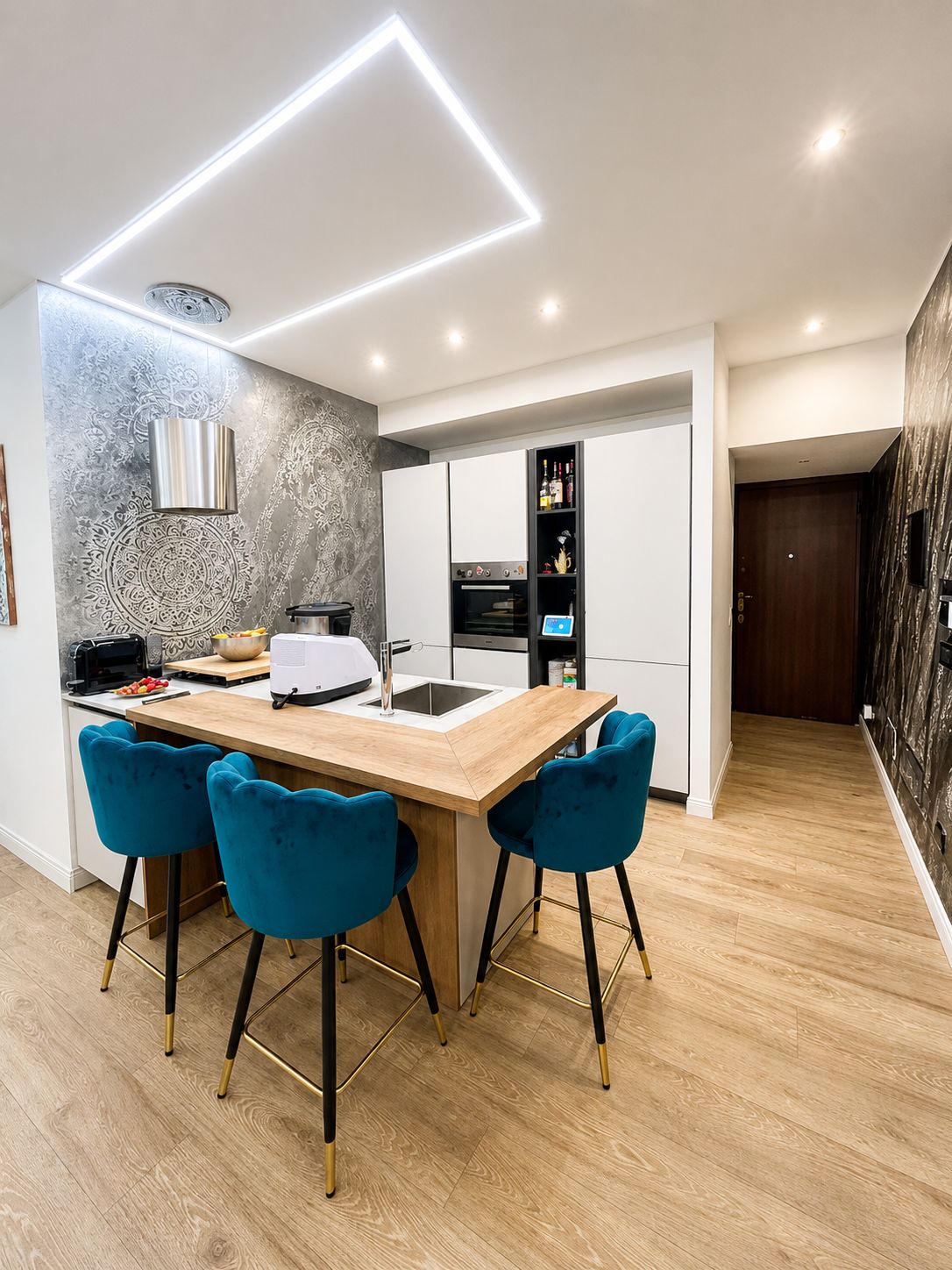 A modern kitchen with a central island, bar stools, and a built-in oven.