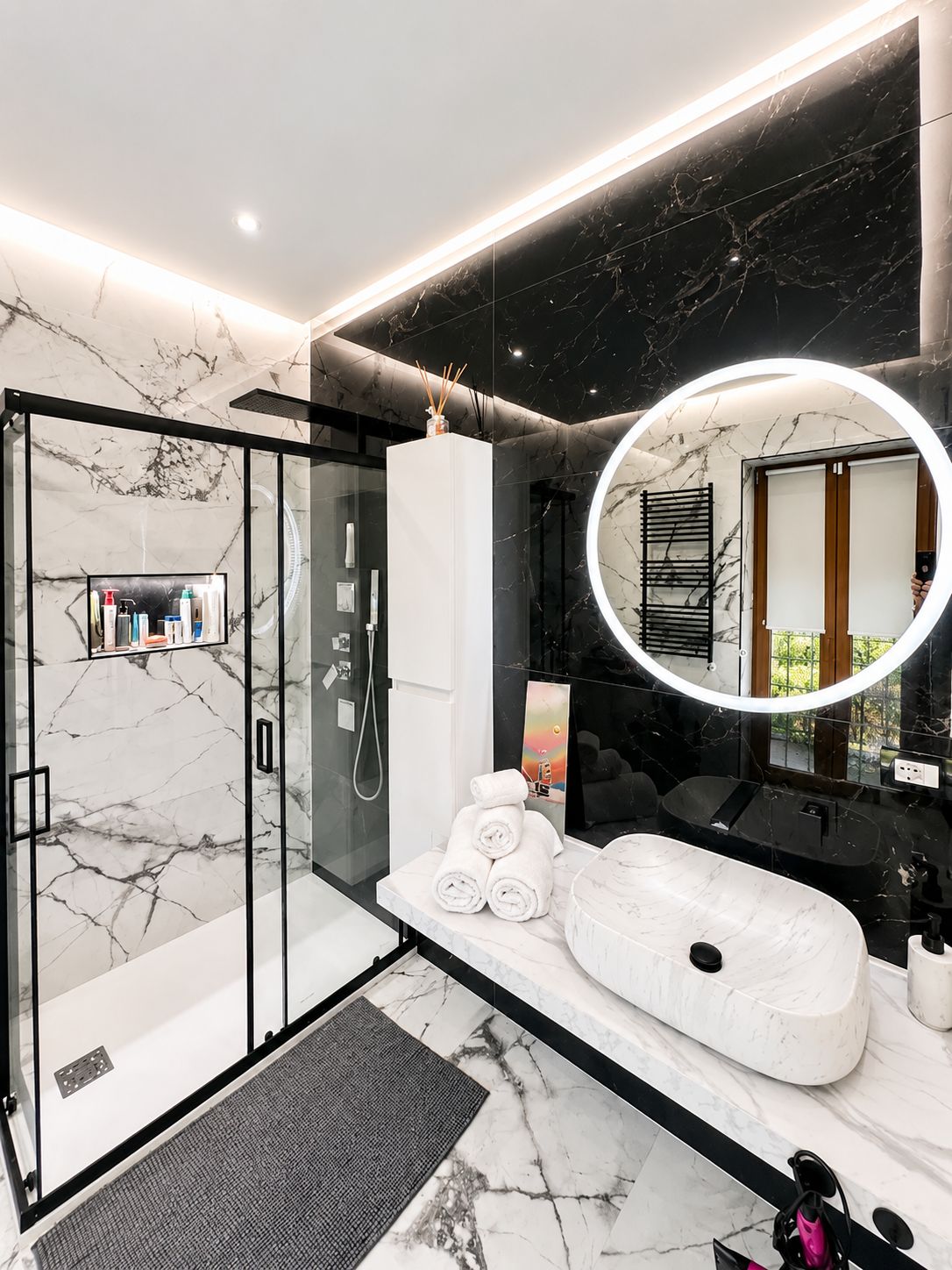 Une salle de bain moderne avec une douche à parois de verre, un sol carrelé en marbre, un grand miroir avec un éclairage circulaire et une baignoire blanche.