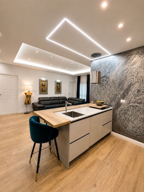 Et moderne køkken med en central ø, et spiseområde med en sofa og en dekorativ væg.