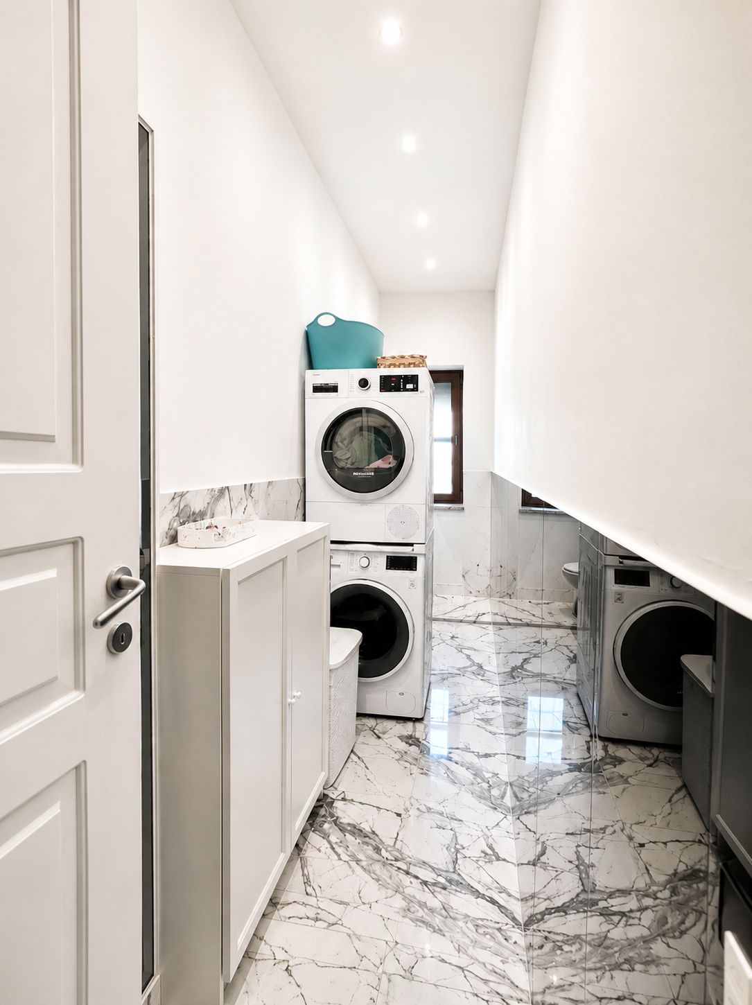 Uma lavanderia com porta branca, máquina de lavar e secadora.
