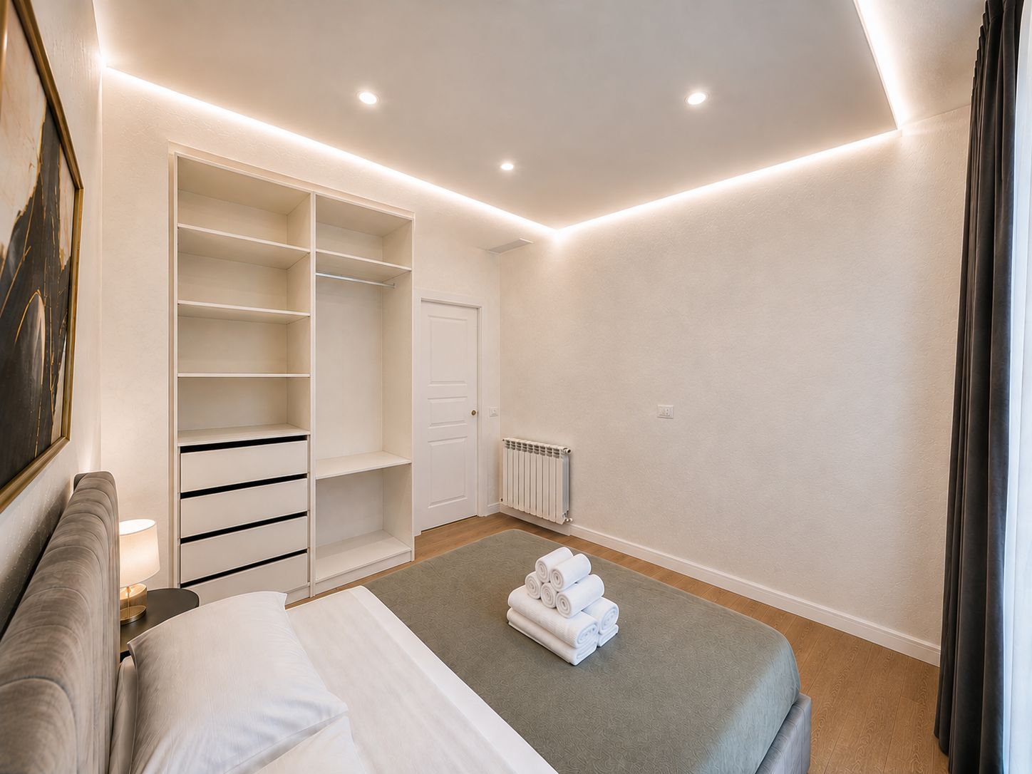 Quarto com cama, armário grande, radiador e mesa de cabeceira com luminária.