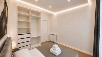 Quarto com cama, armário grande, radiador e mesa de cabeceira com luminária.