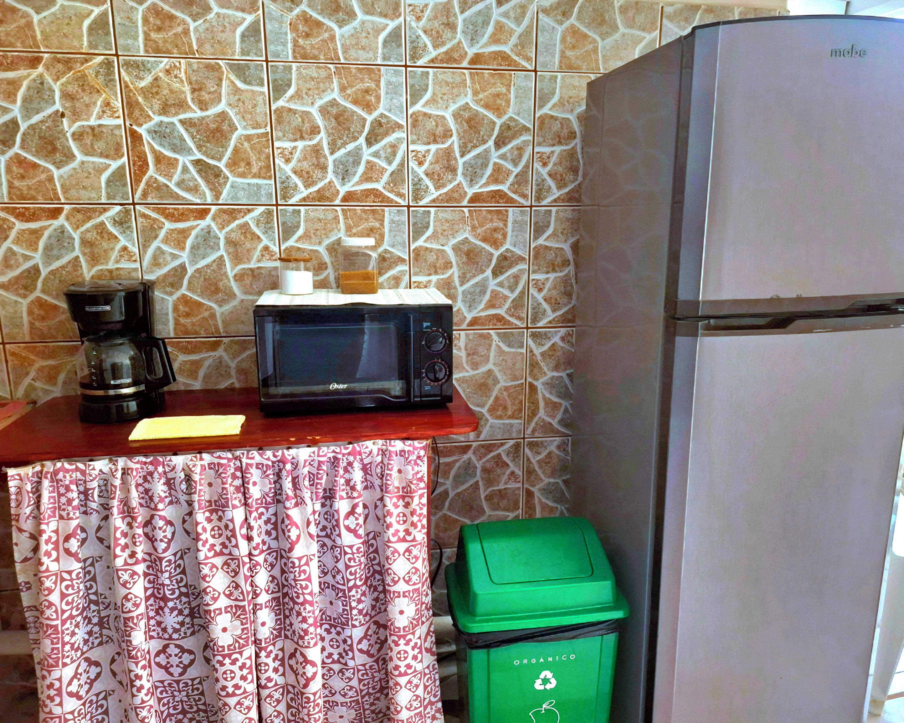Une petite cuisine équipée d’un four à micro-ondes, d’une machine à café et d’une poubelle verte.