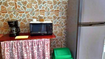 Une petite cuisine équipée d’un four à micro-ondes, d’une machine à café et d’une poubelle verte.