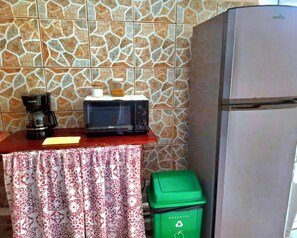 A kitchenette with a microwave, coffee maker, and a green trash bin.