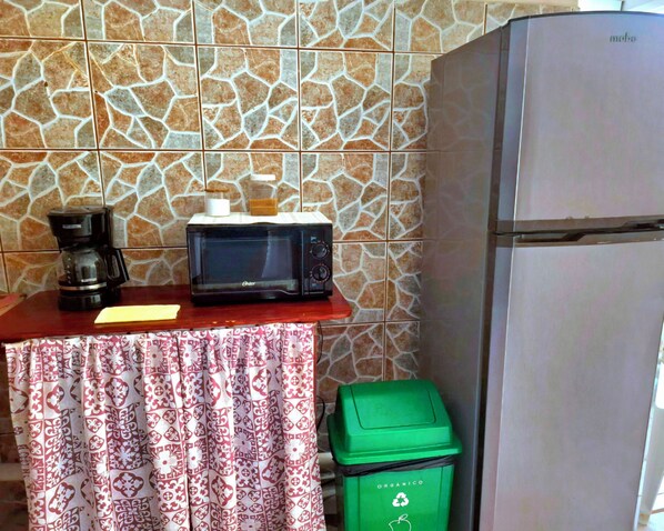 A kitchenette with a microwave, coffee maker, and a green trash bin.