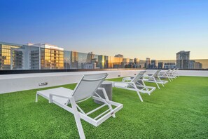 A rooftop terrace with white lounge chairs and artificial grass, overlooking a city skyline with modern buildings. - Modern 1BR | Pool & Gym Access | Downtown Miami (Miami)