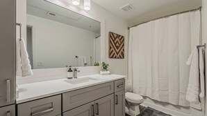 Une salle de bain moderne avec un grand miroir, un lavabo blanc, des toilettes et un rideau de douche.