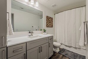 Une salle de bain moderne avec un grand miroir, un lavabo blanc, des toilettes et un rideau de douche.