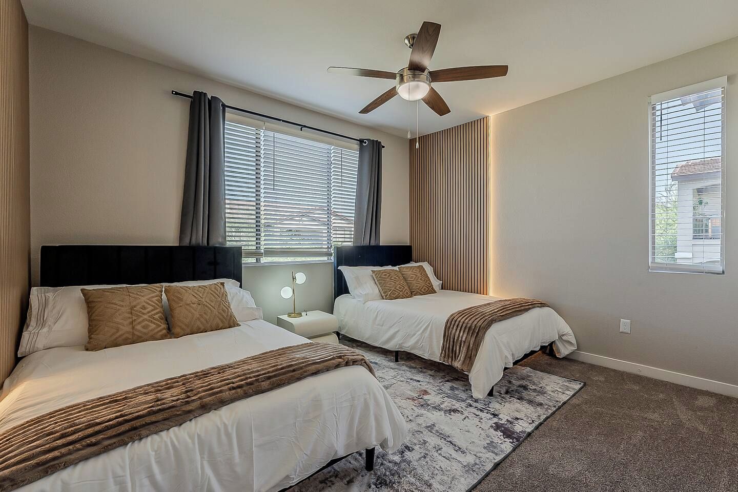 Een hotelkamer met twee bedden, een plafondventilator, een raam met zonwering en een vloerkleed.