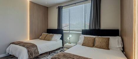 A hotel room with two beds, a ceiling fan, a window with blinds, and a bedside lamp.
