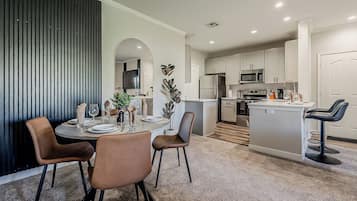 Una cocina moderna con armarios blancos, una isla central y un comedor con una mesa redonda y sillas.