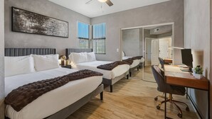 Une chambre d’hôtel avec deux lits, un bureau avec un ordinateur, un ventilateur de plafond et une grande fenêtre avec des stores.