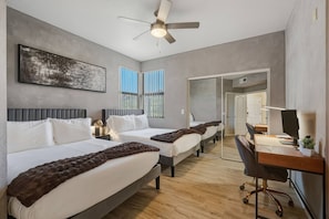 Une chambre d’hôtel avec deux lits, un bureau avec un ordinateur, un ventilateur de plafond et une grande fenêtre avec des stores.