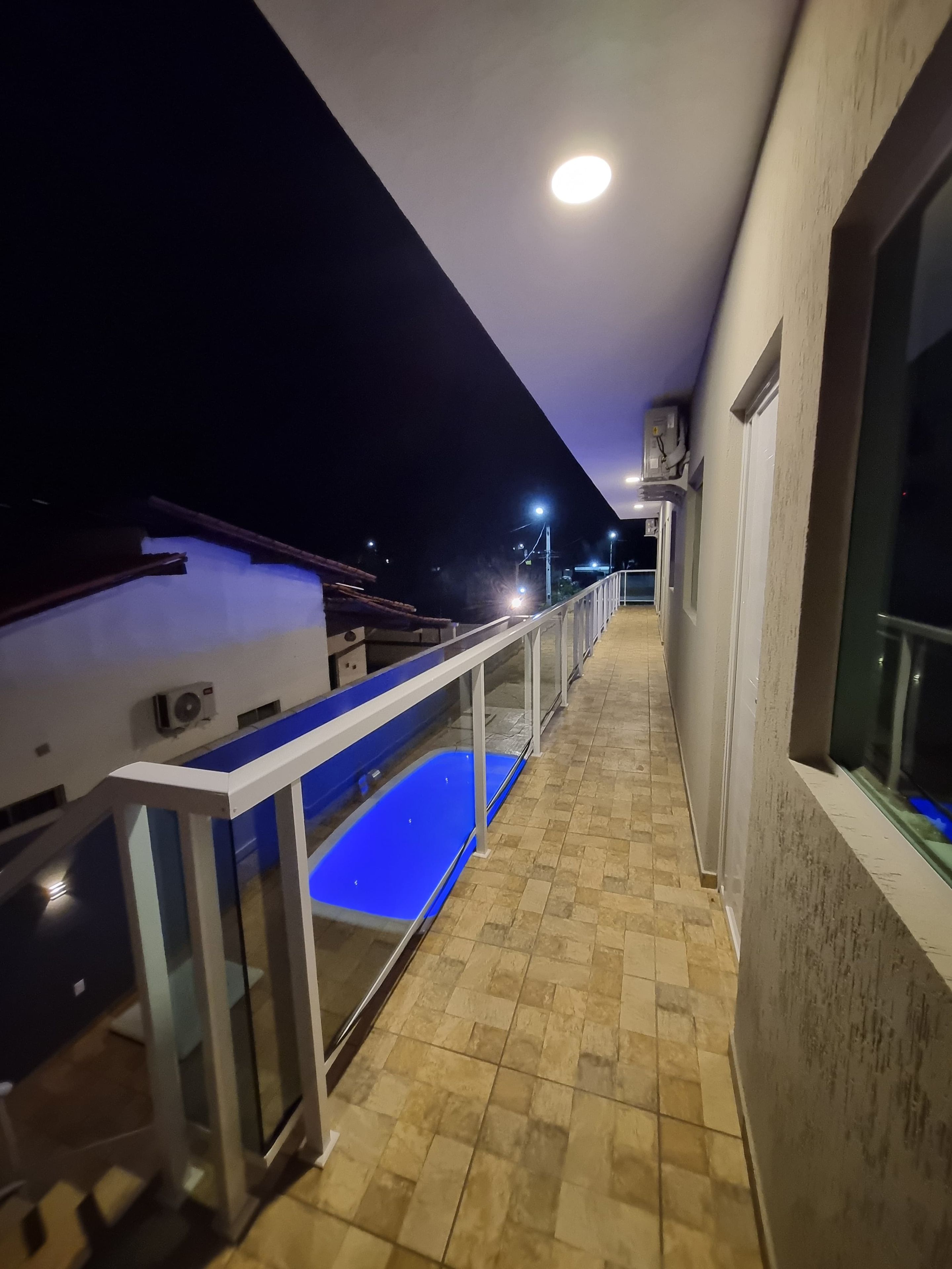 A corridor with a blue-lit pool, a railing, and a ceiling light.