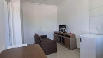 A compact living space with a kitchenette, a dining table, a sofa, and a refrigerator.