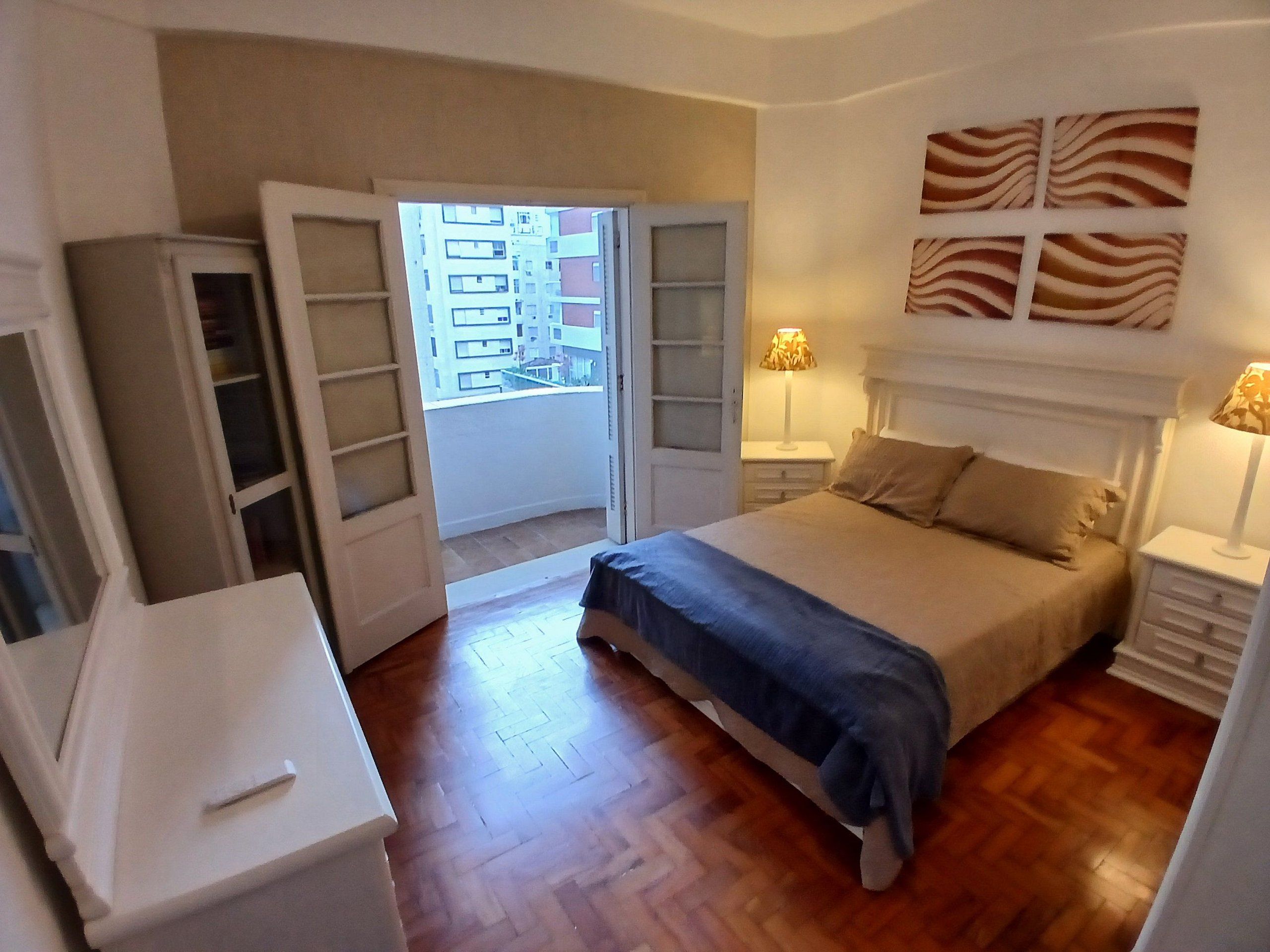 Un dormitorio con cama, mesitas de noche, armario y vistas a través de una puerta abierta.