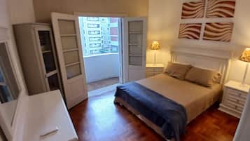 Un dormitorio con cama, mesitas de noche, armario y vistas a través de una puerta abierta.