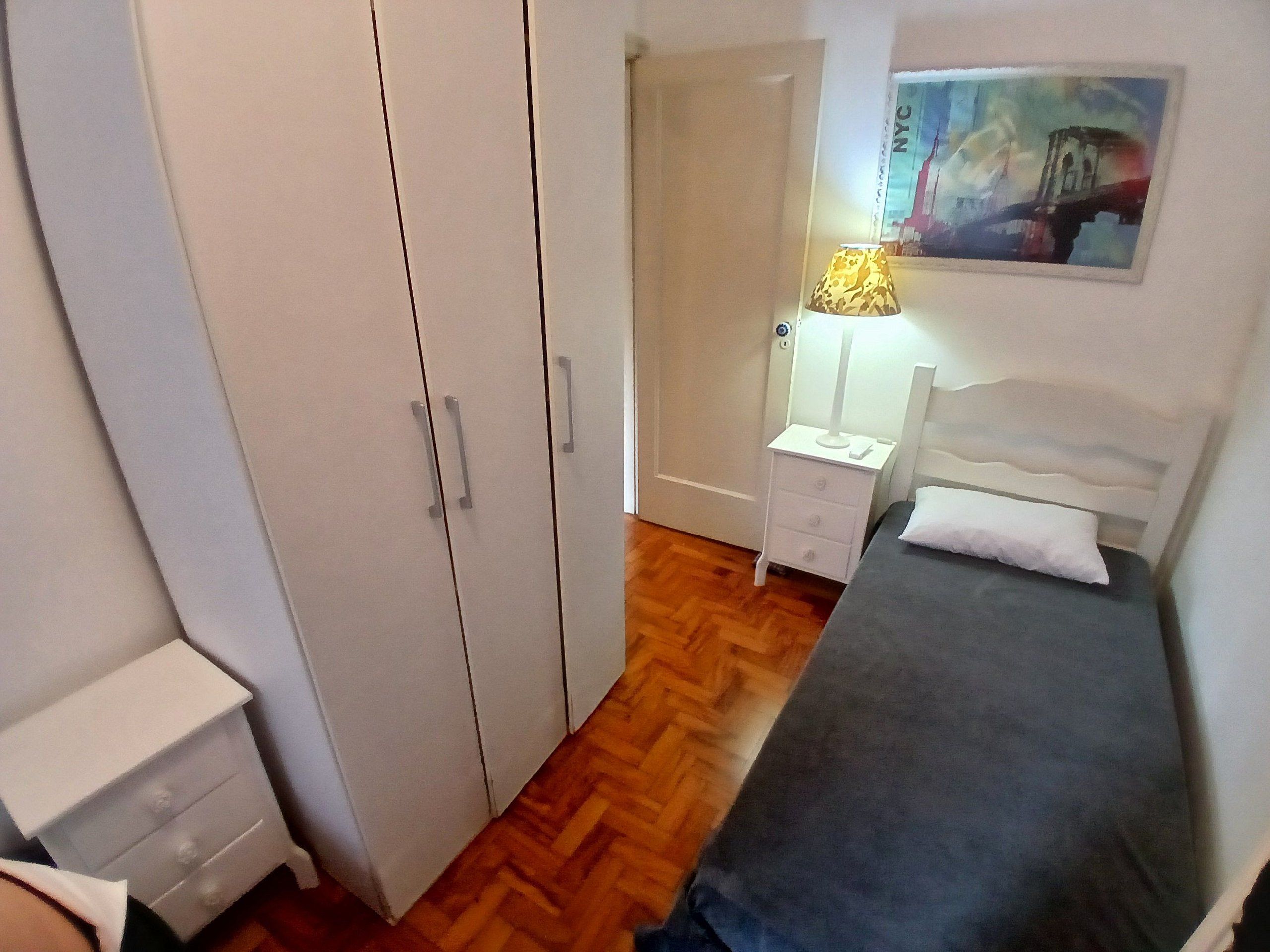 A bedroom with a bed, a nightstand, a wardrobe, and a painting on the wall.