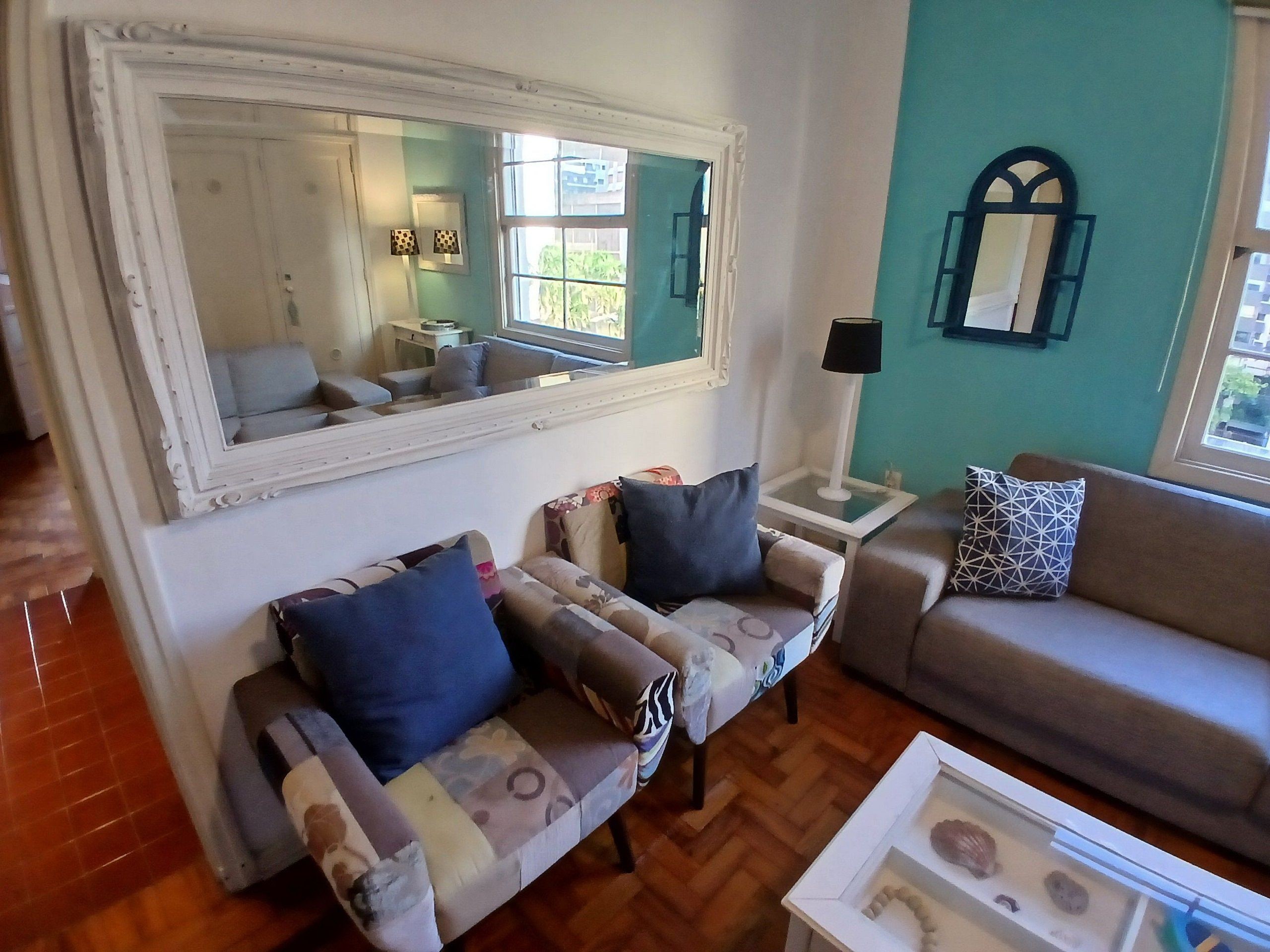 A living room with a large mirror, two sofas, a side table with a lamp, and a window with a view.